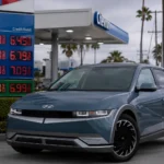 سيارة هيونداي Ioniq 5 الكهربائية متوقفة بجوار محطة وقود تعرض أسعار بنزين مرتفعة، في مشهد يعكس توجه المستهلكين نحو السيارات الكهربائية بسبب أزمة الوقود.
