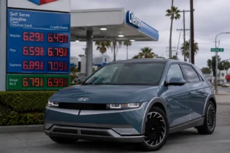 سيارة هيونداي Ioniq 5 الكهربائية متوقفة بجوار محطة وقود تعرض أسعار بنزين مرتفعة، في مشهد يعكس توجه المستهلكين نحو السيارات الكهربائية بسبب أزمة الوقود.