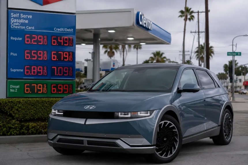 سيارة هيونداي Ioniq 5 الكهربائية متوقفة بجوار محطة وقود تعرض أسعار بنزين مرتفعة، في مشهد يعكس توجه المستهلكين نحو السيارات الكهربائية بسبب أزمة الوقود.