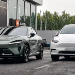 سيارة Xiaomi YU7 الكهربائية الجديدة بجانب Tesla Model Y أمام مبنى حديث في مقارنة توضح التصميم والمنافسة بين السيارتين الكهربائيتين.