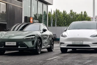 سيارة Xiaomi YU7 الكهربائية الجديدة بجانب Tesla Model Y أمام مبنى حديث في مقارنة توضح التصميم والمنافسة بين السيارتين الكهربائيتين.