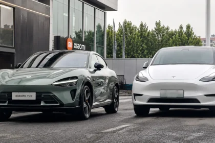 سيارة Xiaomi YU7 الكهربائية الجديدة بجانب Tesla Model Y أمام مبنى حديث في مقارنة توضح التصميم والمنافسة بين السيارتين الكهربائيتين.