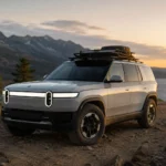 سيارة ريفيان R2 الجديدة متوقفة على طريق جبلي وعر أثناء غروب الشمس، وتُظهر تصميم SUV عصري وقدرات مخصصة للمغامرات والطرق الوعرة.